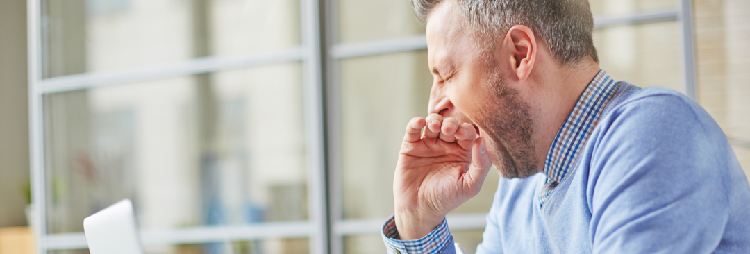 A tired middle-aged man yawning at his desk, illustrating the fatigue that magnesium supplements can help alleviate.