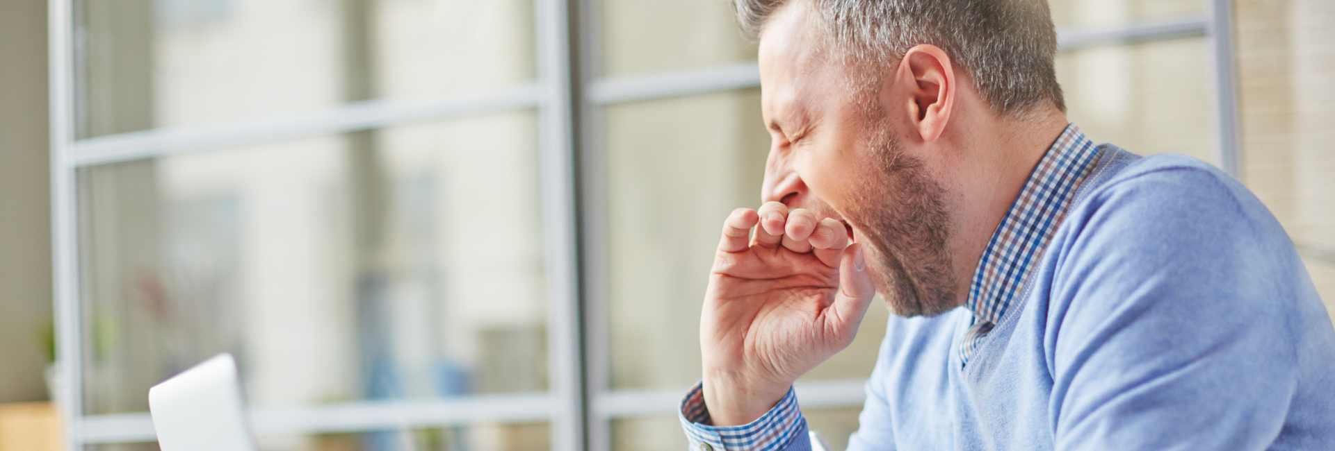 A tired middle-aged man yawning at his desk, illustrating the fatigue that magnesium supplements can help alleviate.