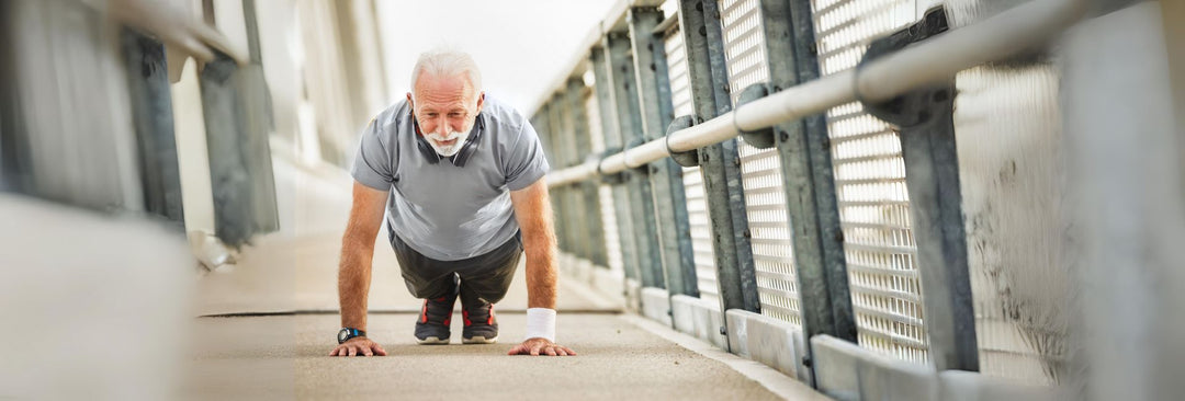 Older man doing push ups on the sidewalk of a bridge. 
